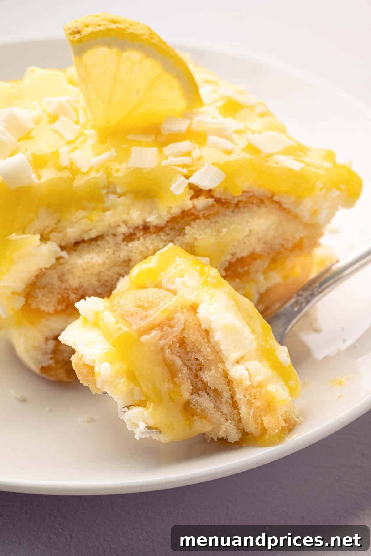 Bright Citrus Tiramisu 2 A fork taking a bite out of limoncello tiramisu with a slice on a white plate, highlighting its creamy layers and bright yellow hue.