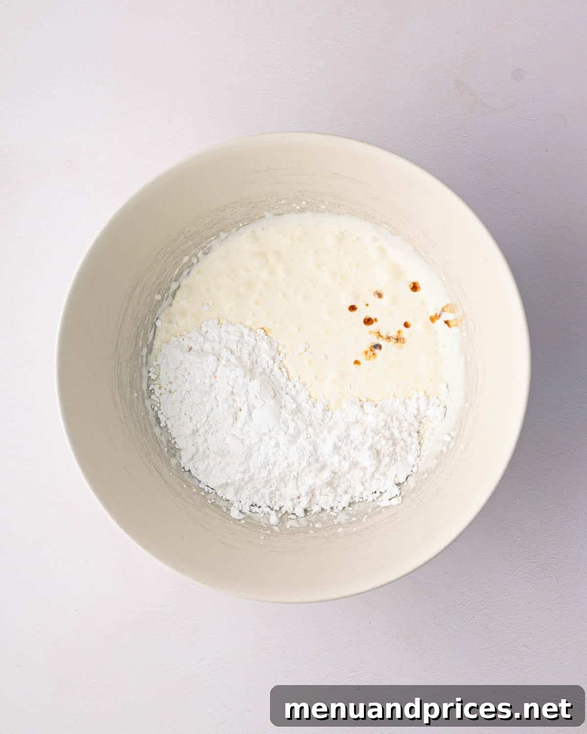 Bright Citrus Tiramisu 11 A white mixing bowl containing cold heavy whipping cream, powdered sugar, and vanilla extract.