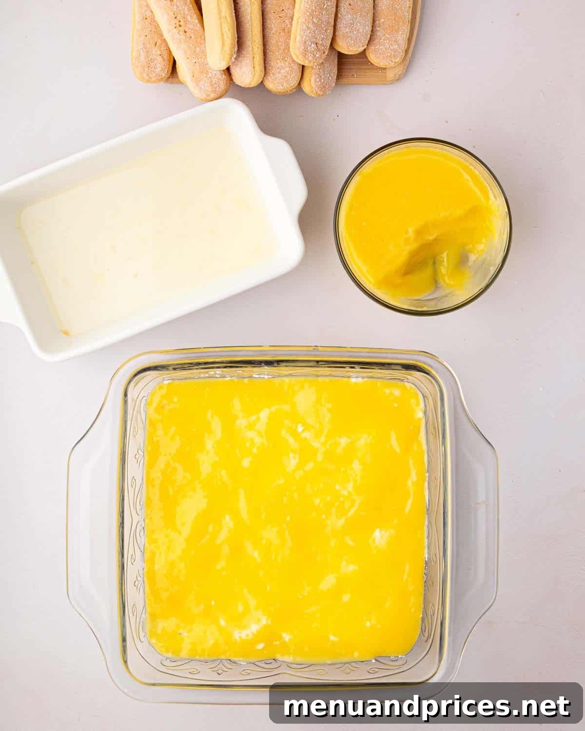 Bright Citrus Tiramisu 18 A glass baking dish showcasing a layer of vibrant lemon curd spread over mascarpone cream and ladyfingers, with a bowl of extra lemon curd on the side.