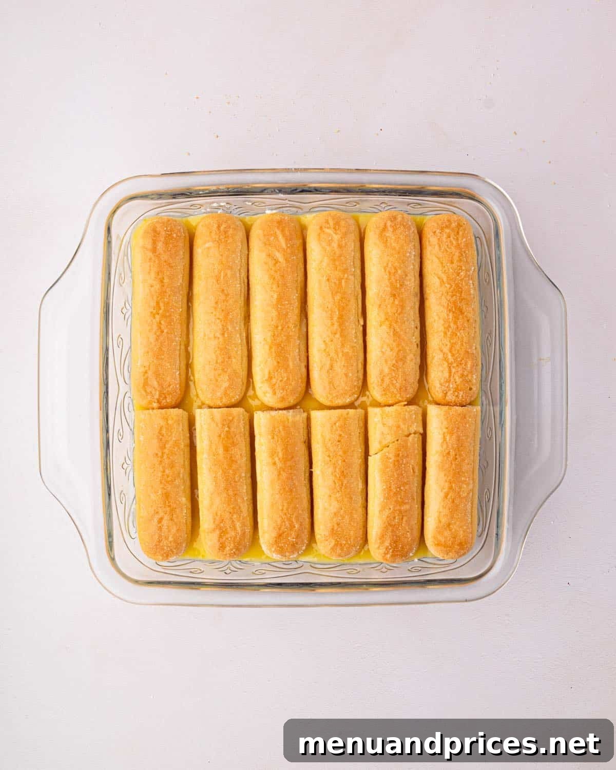 Bright Citrus Tiramisu 19 A glass baking dish revealing the multiple layers of lemon curd, mascarpone cream, and soaked ladyfingers within the tiramisu structure.