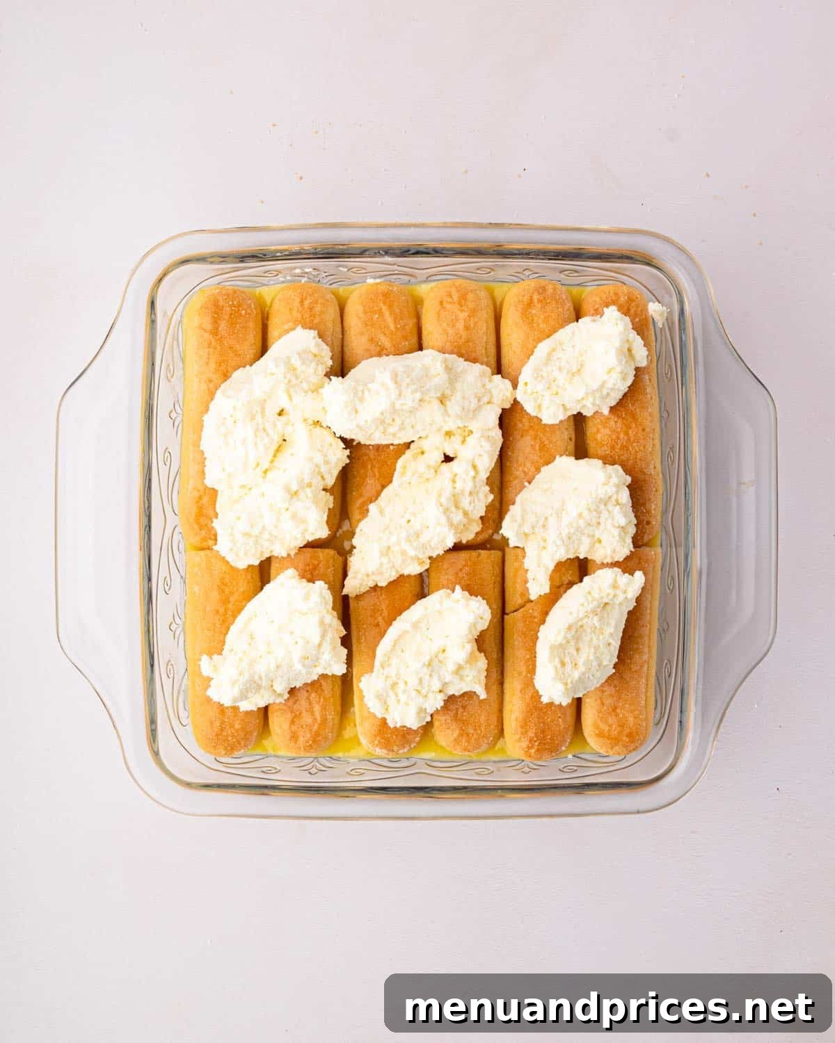 Bright Citrus Tiramisu 20 A glass baking dish filled with tiramisu layers, topped with dollops of mascarpone whipped cream, ready for the final lemon curd layer.