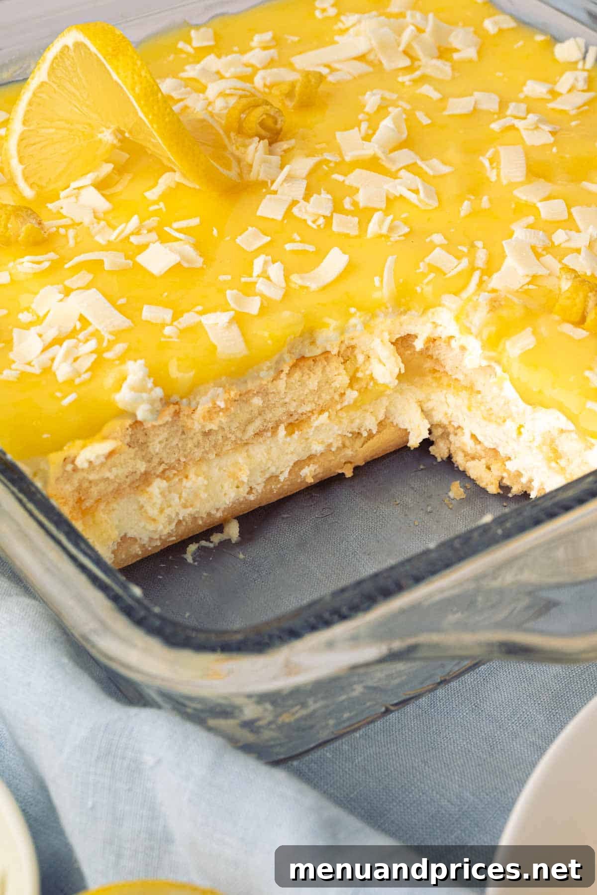 Bright Citrus Tiramisu 3 A glass baking dish with a perfectly portioned slice taken out of the lemon tiramisu, revealing the distinct layers of ladyfingers, lemon curd, and mascarpone cream.