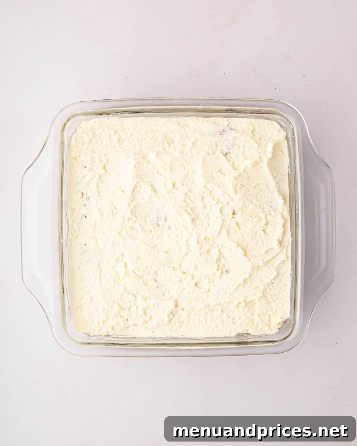 Bright Citrus Tiramisu 21 The final layer of mascarpone whipped cream being spread smoothly over the top of the lemon tiramisu in a glass baking dish.