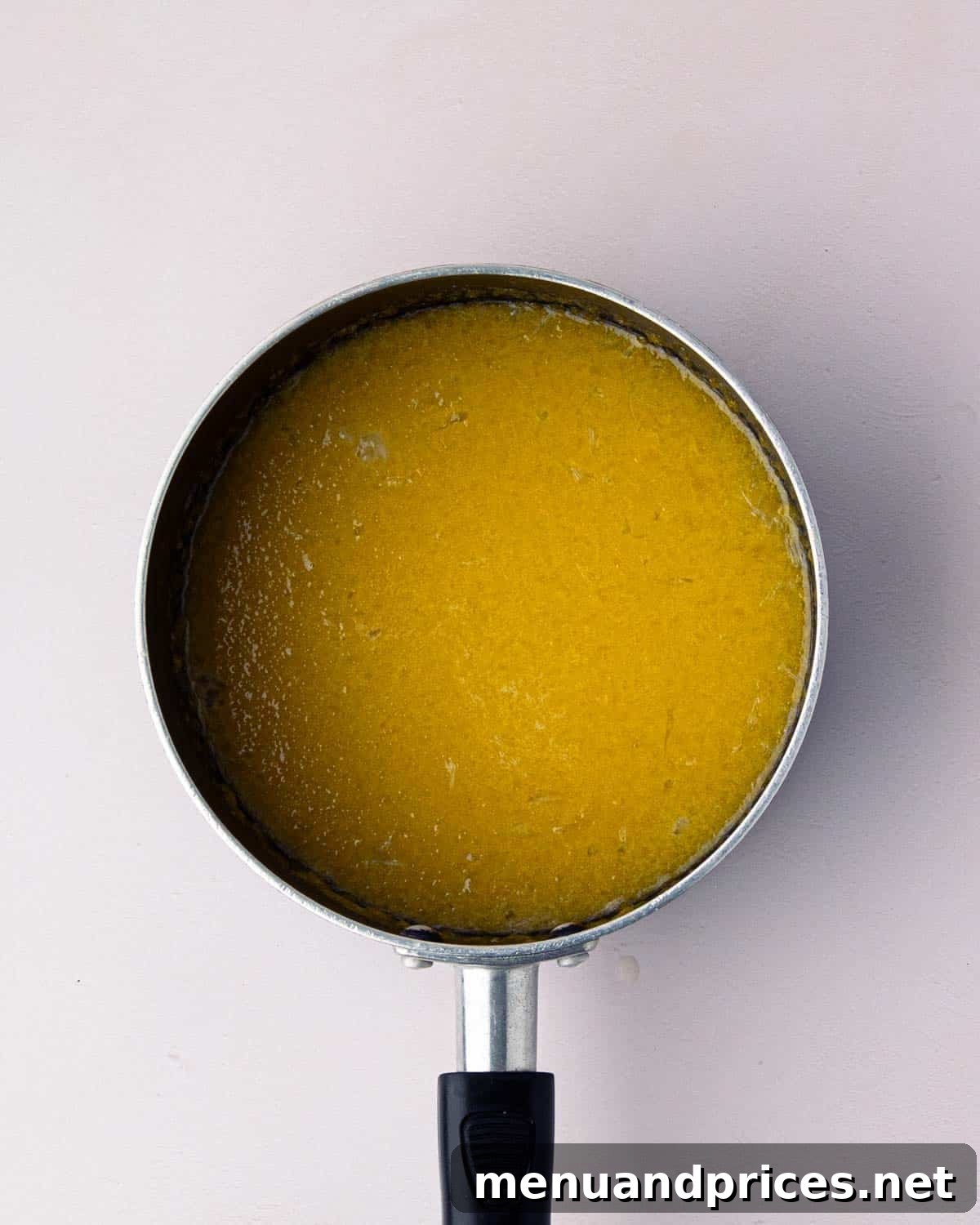 Bright Citrus Tiramisu 6 Lemon curd mixture gently simmering in a black saucepan, with a whisk nearby, illustrating the cooking process.
