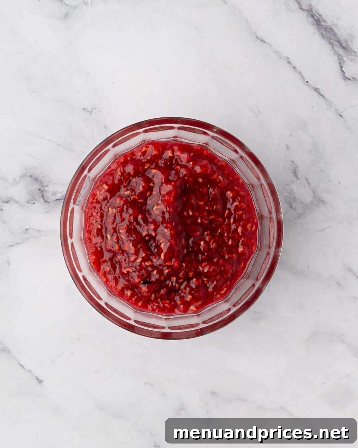 Cooled raspberry compote in a clear glass bowl, showcasing its rich texture.