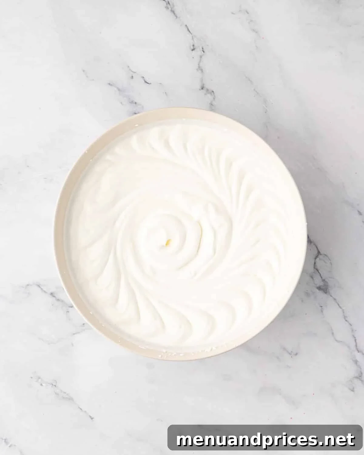 Freshly whipped cream with soft peaks in a white mixing bowl.