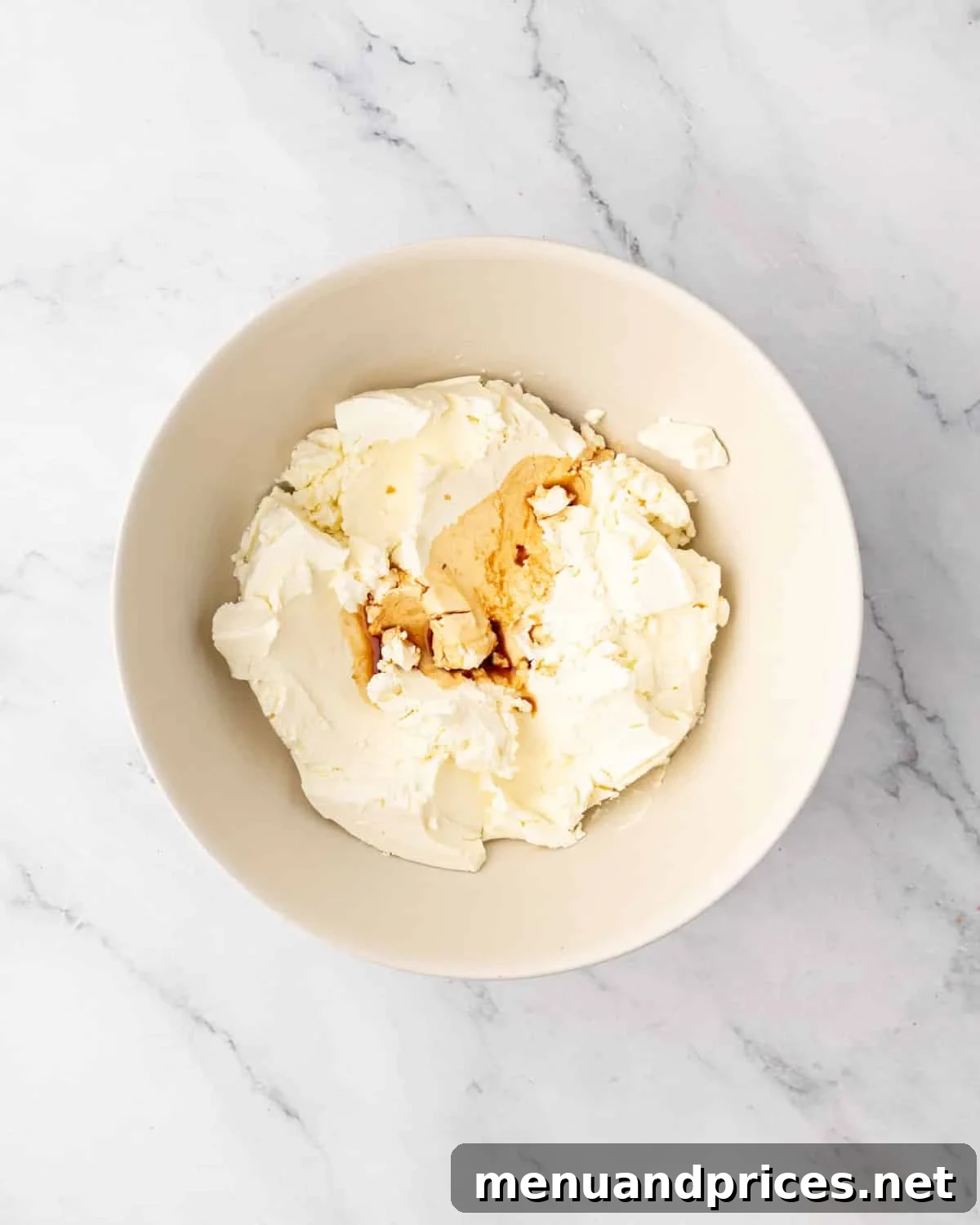 Mascarpone cheese and vanilla extract in a white bowl, before whisking.