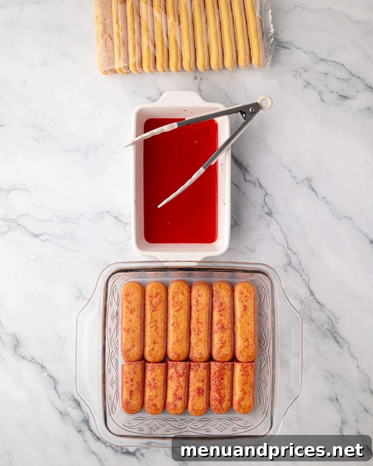 Ladyfingers, lightly soaked in raspberry simple syrup, forming the first layer in a glass baking dish.