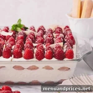 Side image of raspberry tiramisu in a glass baking dish, garnished with fresh berries.