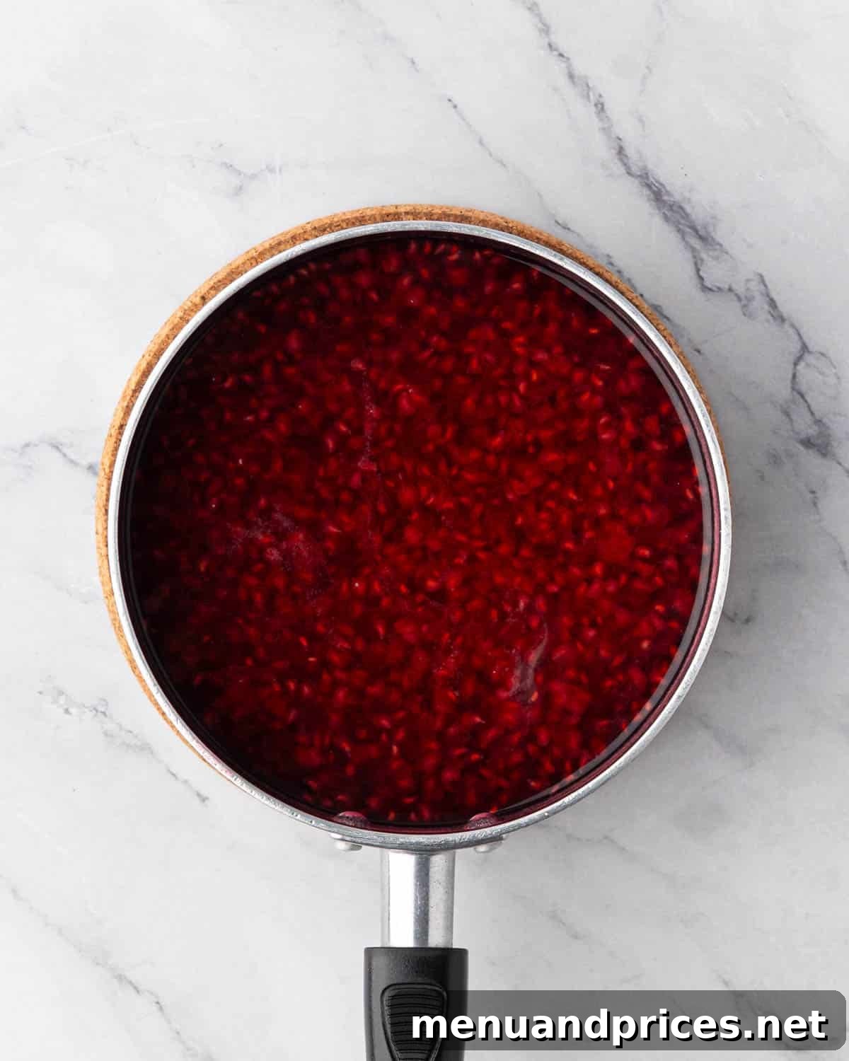 Raspberry simple syrup simmering in a black saucepan, turning a deep red color.