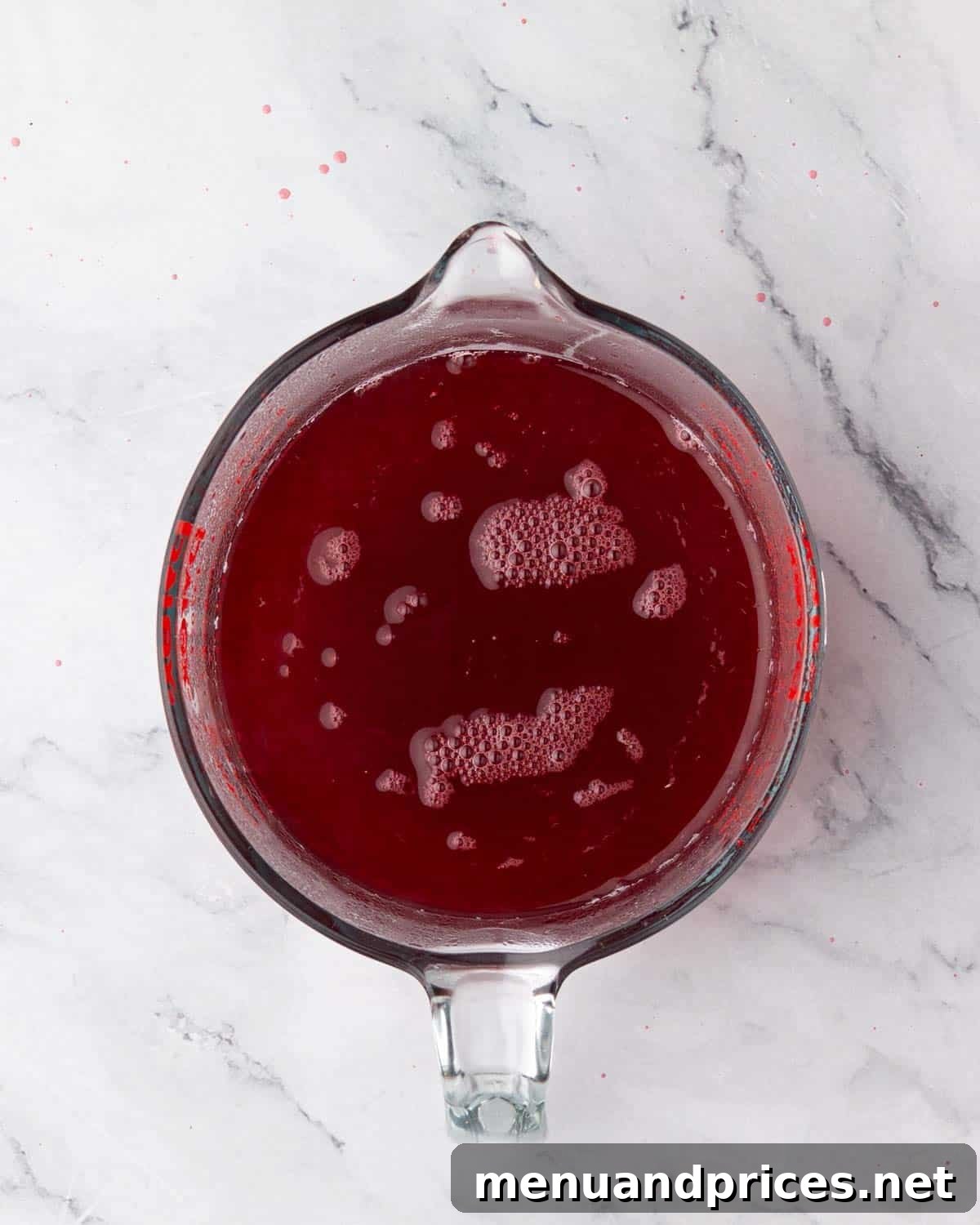 Cooled raspberry simple syrup in a glass measuring cup, ready for assembly.
