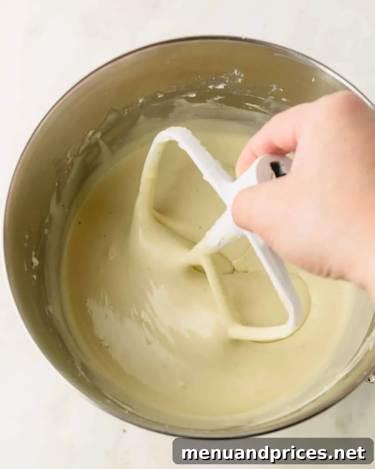 A hand is adding the paddle attachment to the stand mixer with the pistachio cheesecake filling.