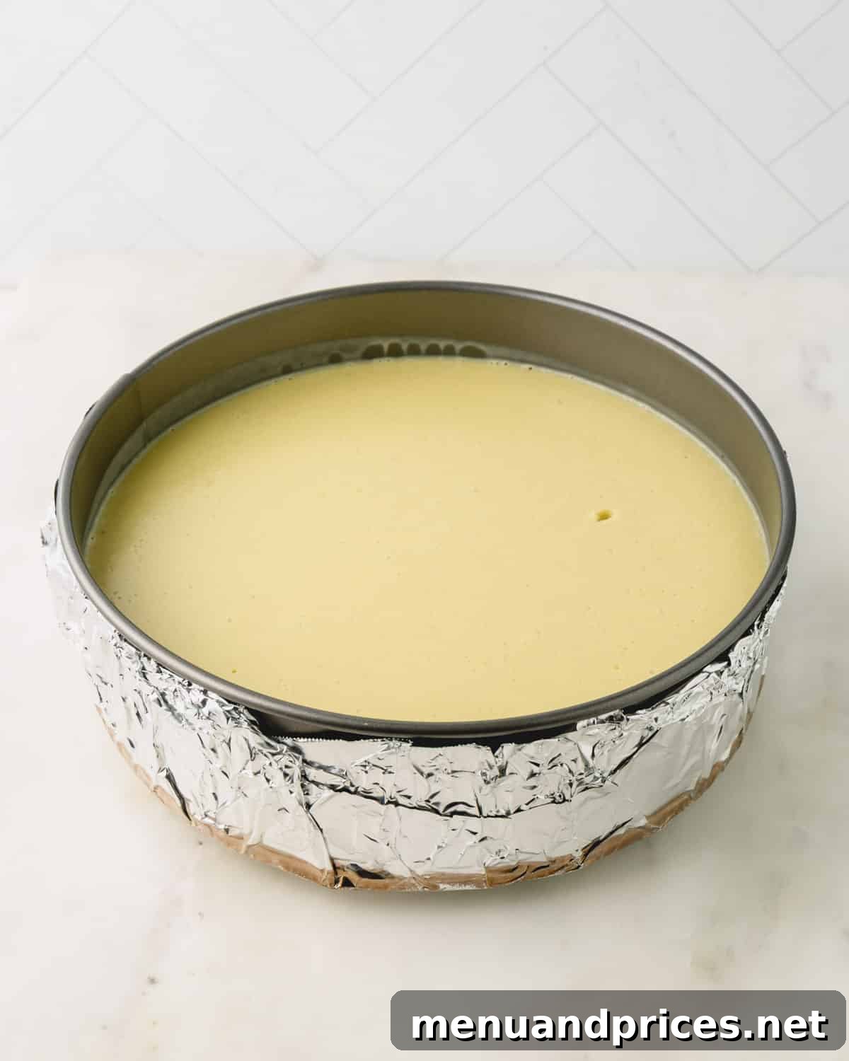 A springform pan with pistachio cheesecake ready to bake. The pan is wrapped in foil.