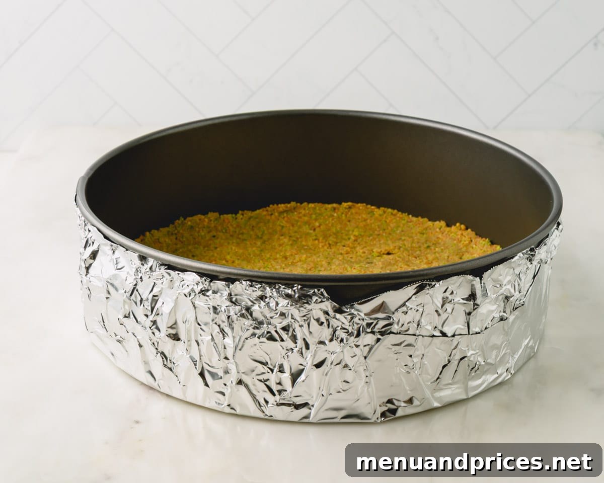Pistachio graham cracker crust in a springform pan with foil wrapped around the bottom.