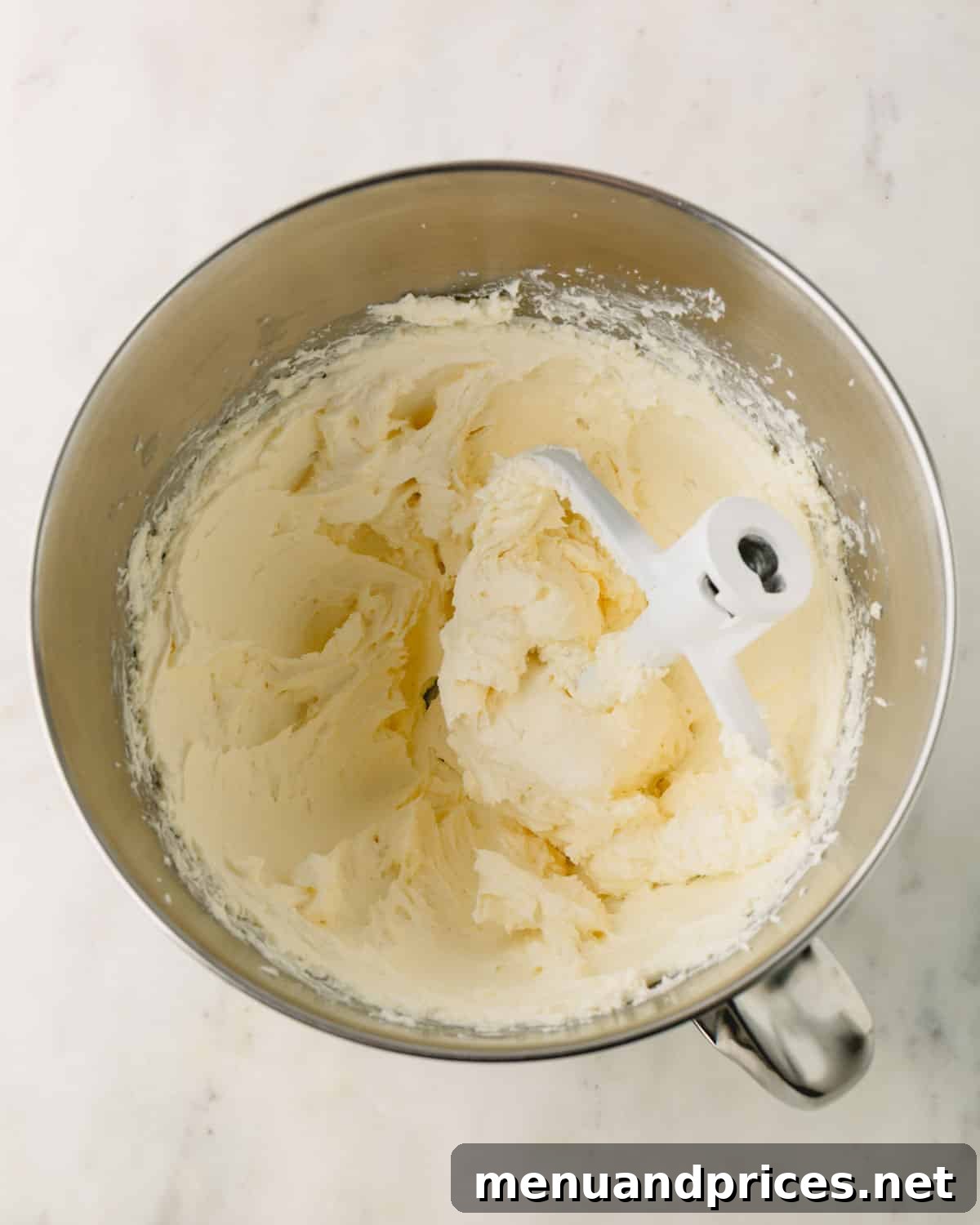 A stand mixer with cream cheese filling for cheesecake and a paddle attachment resting in the bowl.