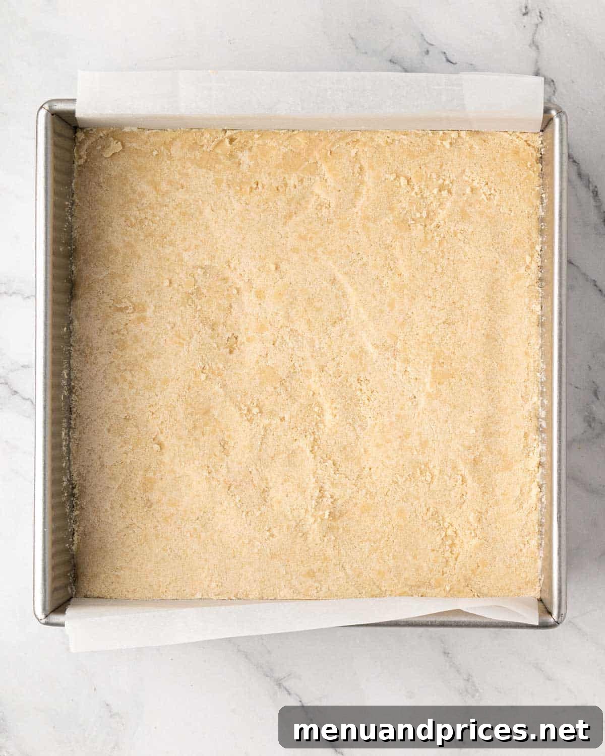 Shortbread cookie mixture pressed into the bottom of a baking dish lined with parchment.