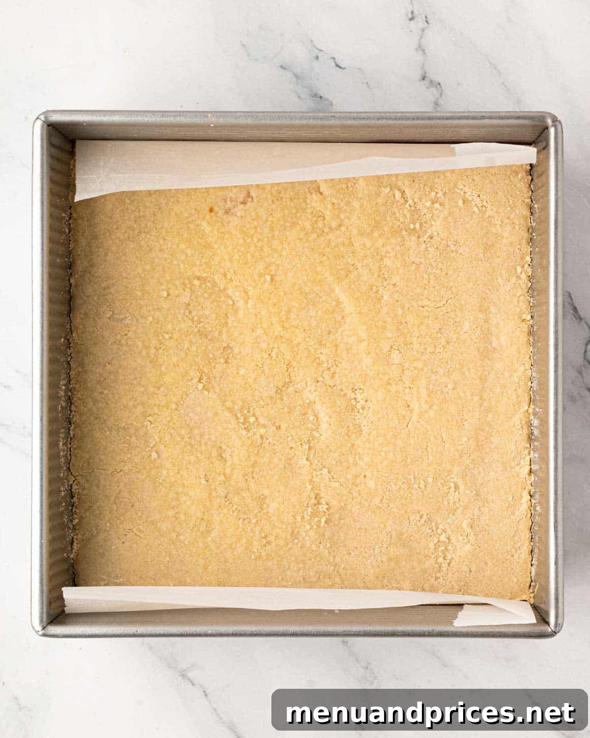 A baking pan with shortbread cookie pressed in the bottom and lined with parchment.