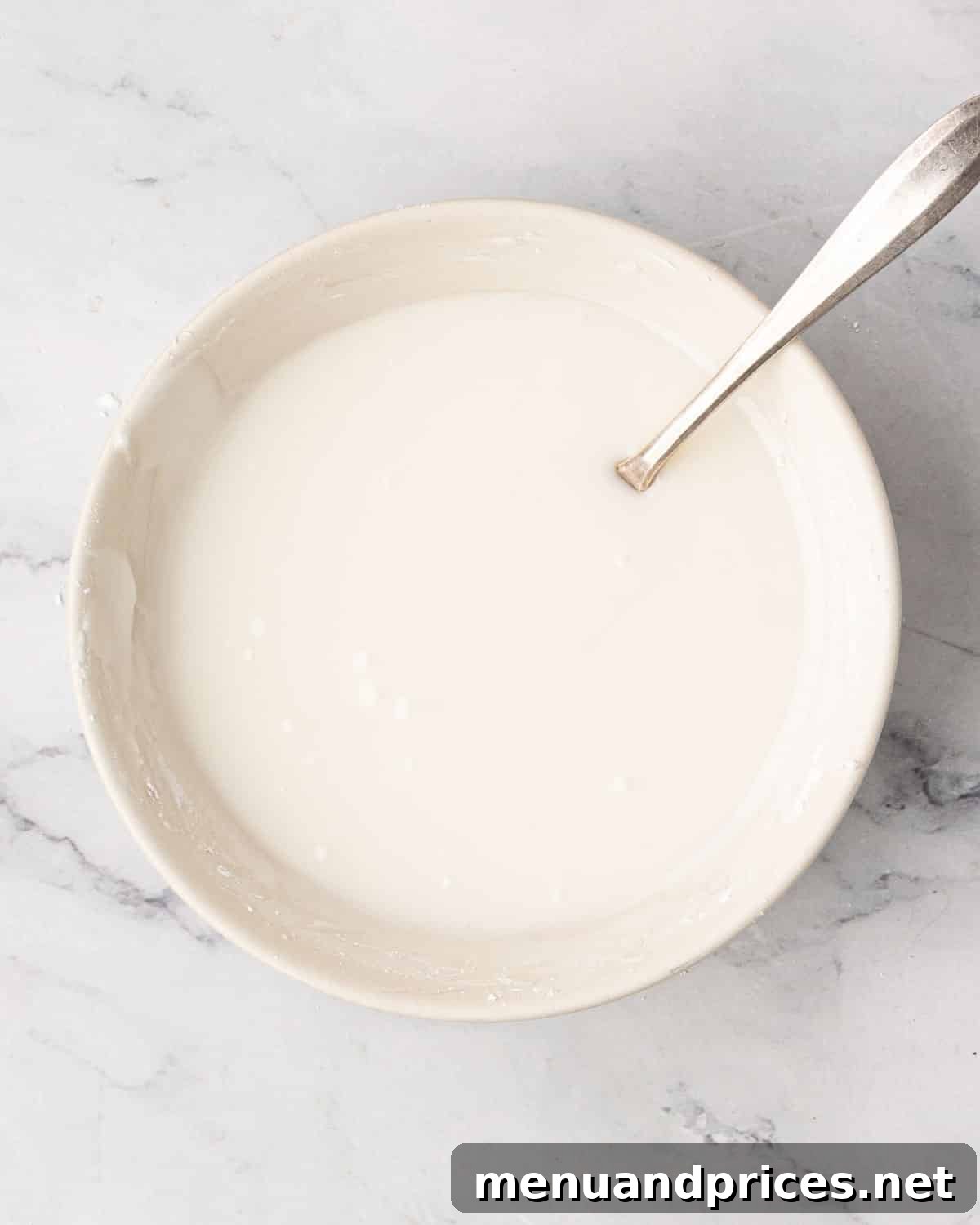 A white bowl with mixed icing and a spoon resting on the side.