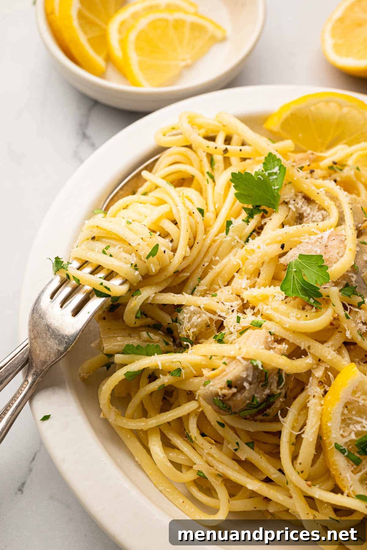 Lemon Artichoke Pasta with Garlic, Parmesan and Herbs 11 A close up image of lemon artichoke pasta with a fork and spoon in a white bowl.